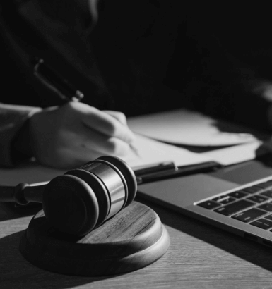 Um homem escrevendo em uma prancheta, um notebook na sua frente e um martelo de juiz do seu lado